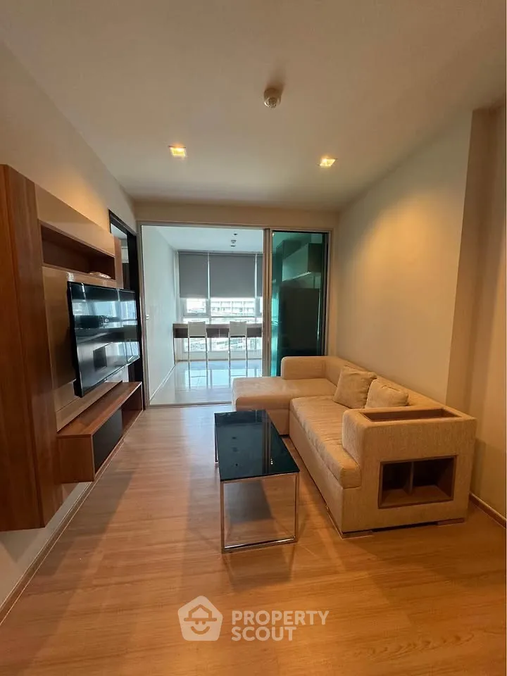 Modern living room with cozy sofa and sleek TV unit, leading to a bright balcony with city views.