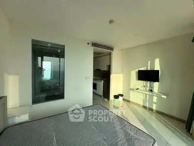 Modern bedroom with integrated kitchenette and wall-mounted TV, featuring a large window for natural light.