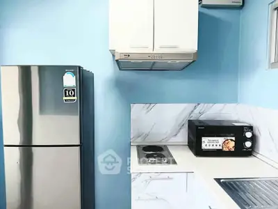 Modern kitchen with stainless steel fridge, microwave, and sleek cabinetry in a compact layout.