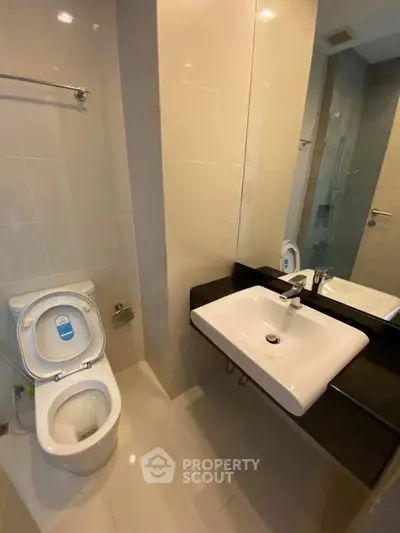 Modern bathroom with sleek fixtures and neutral tiles, featuring a contemporary sink and toilet.