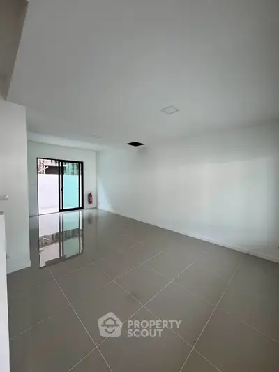 Spacious empty living room with glossy tiled floors and sliding glass doors leading to a patio.