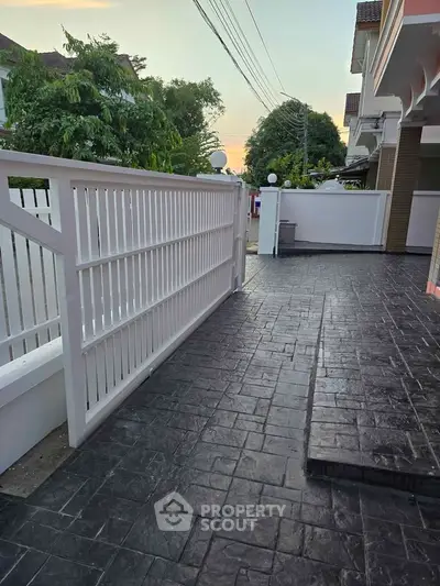 Charming residential entrance with elegant white gate and textured stone pathway at sunset.