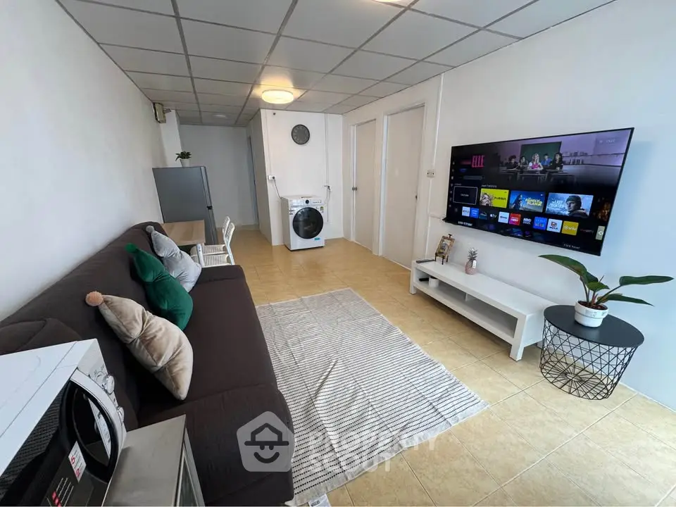 Modern living room with sleek TV setup and cozy seating area, featuring a washing machine and minimalist decor.