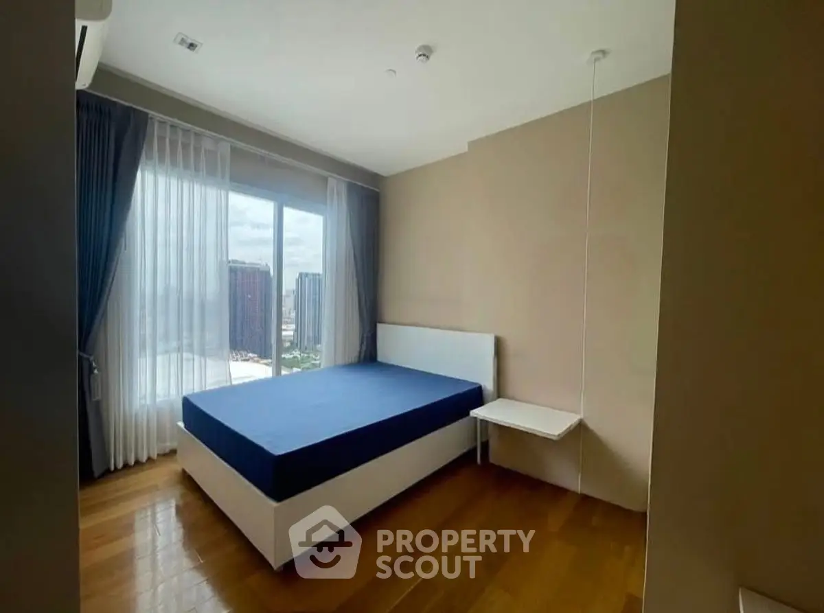 Modern bedroom with large window and wooden flooring in high-rise apartment.