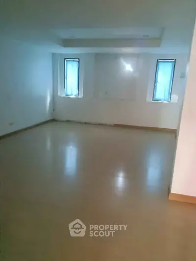 Spacious empty room with two windows and wooden flooring, ideal for customization.