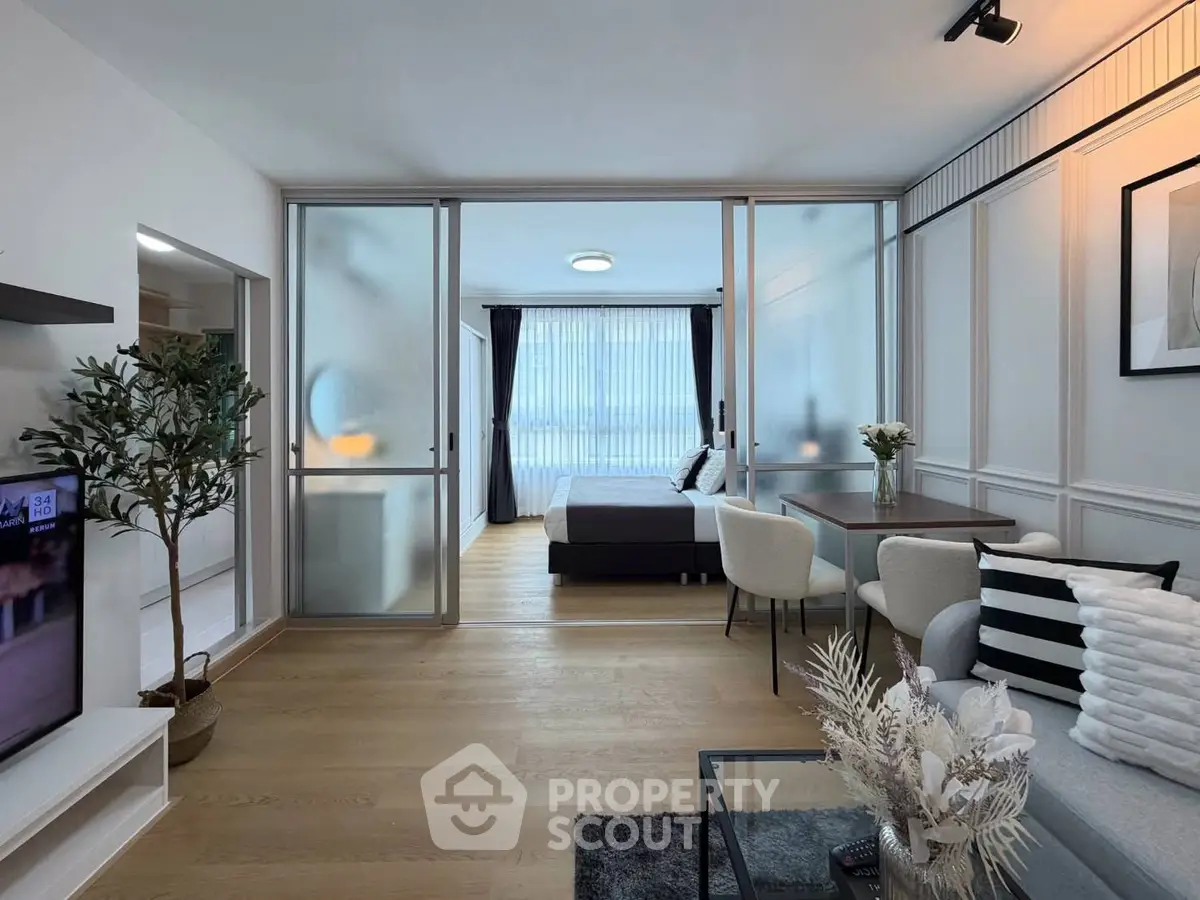 Modern open-plan living room with sliding glass doors leading to a stylish bedroom, featuring elegant decor and natural light.