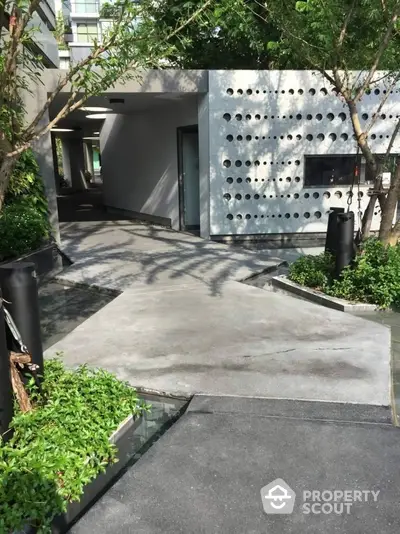 Modern building entrance with unique perforated wall design and lush greenery