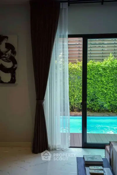 Luxurious living room with pool view through elegant sliding glass doors and lush greenery.