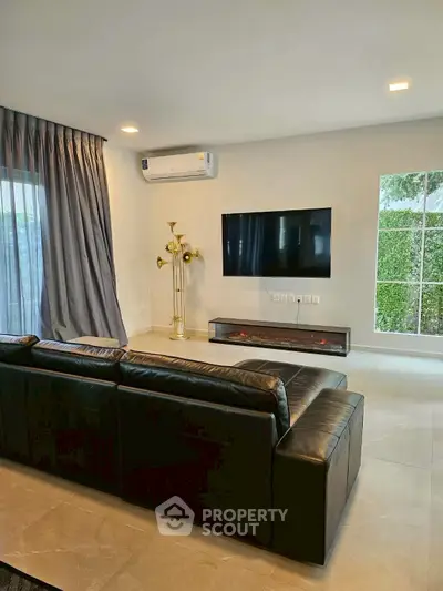 Modern living room with sleek black sofa, wall-mounted TV, and large window view.