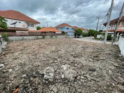 Vacant land plot in residential area with potential for development, surrounded by houses under cloudy sky.