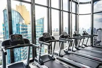 Modern gym with city view in high-rise building, featuring multiple treadmills and large windows.