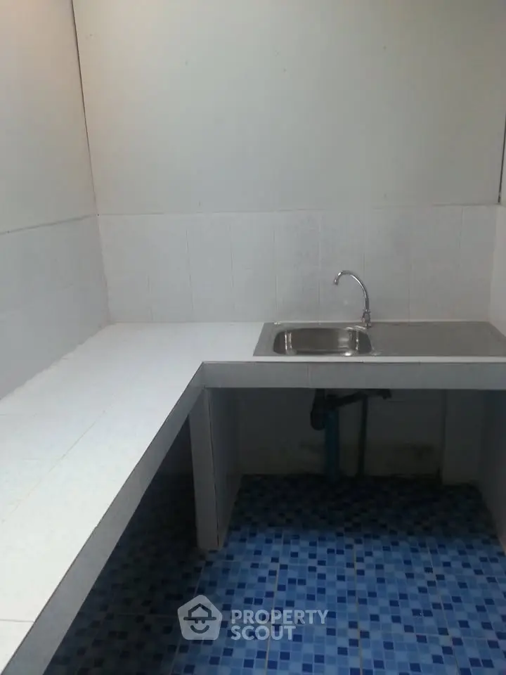 Compact kitchen area with tiled countertop and sink, featuring blue mosaic floor tiles.