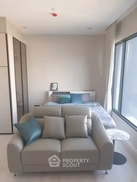 Modern studio apartment with cozy sofa and bed, large windows, and stylish decor.