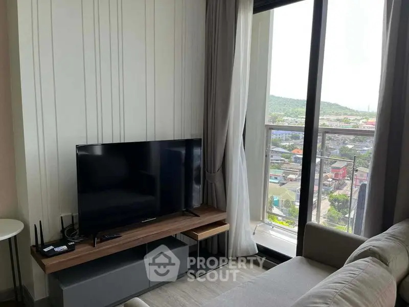 Modern living room with large window offering scenic city view, featuring sleek TV setup and cozy sofa.