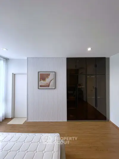 Modern bedroom with sleek wardrobe and minimalist decor, featuring a stylish wall art piece.