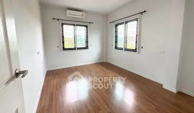 Spacious empty bedroom with wooden flooring and large windows for natural light.