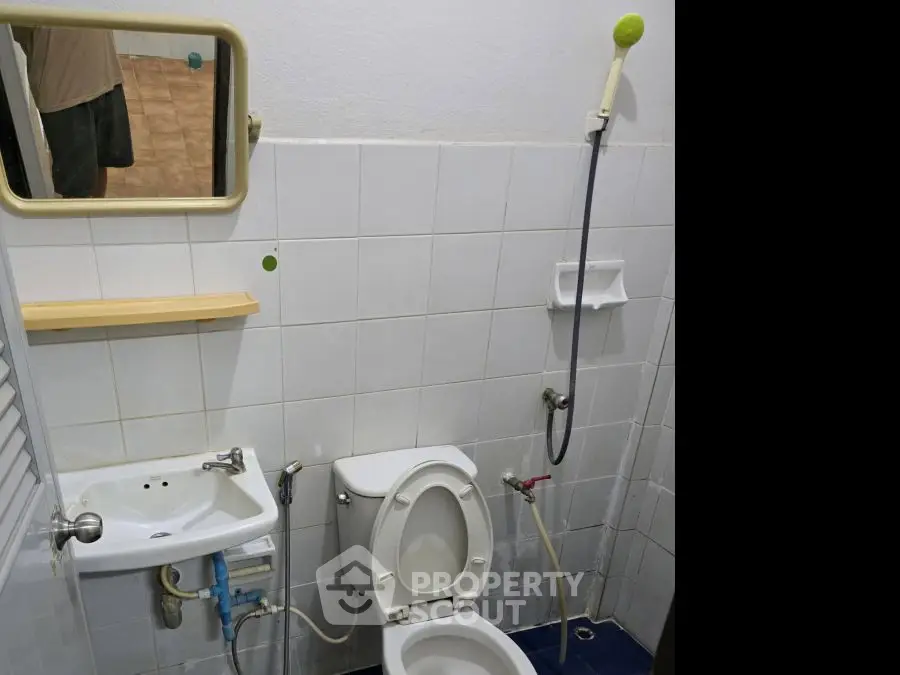 Compact bathroom with white tiles, toilet, sink, and showerhead in a cozy real estate listing.