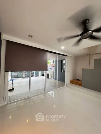 Spacious living room with large sliding glass doors leading to a balcony, featuring a ceiling fan and modern design.