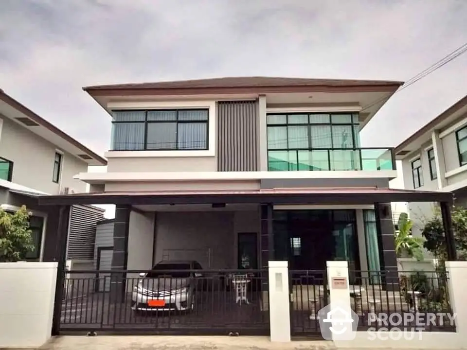 Modern two-story house with large windows and covered parking area in suburban neighborhood.