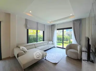 Spacious modern living room with large windows and elegant furniture, offering a serene garden view.