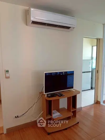 Modern living room with air conditioning and compact TV setup, adjacent to a bright kitchen area.