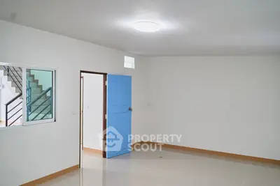 Spacious unfurnished room with blue door and staircase view, ideal for customization.