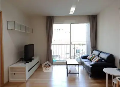 Modern living room with large window and balcony view, featuring sleek furniture and wooden flooring.
