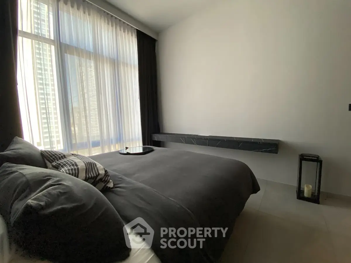 Modern bedroom with large window and stylish decor in urban apartment.