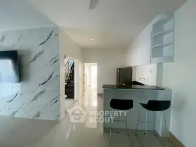 Modern open-plan kitchen with sleek bar stools and marble accent wall