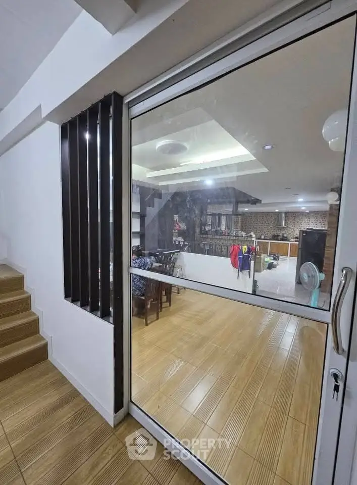 Modern interior with glass door and wooden flooring, showcasing a spacious living area with dining setup.