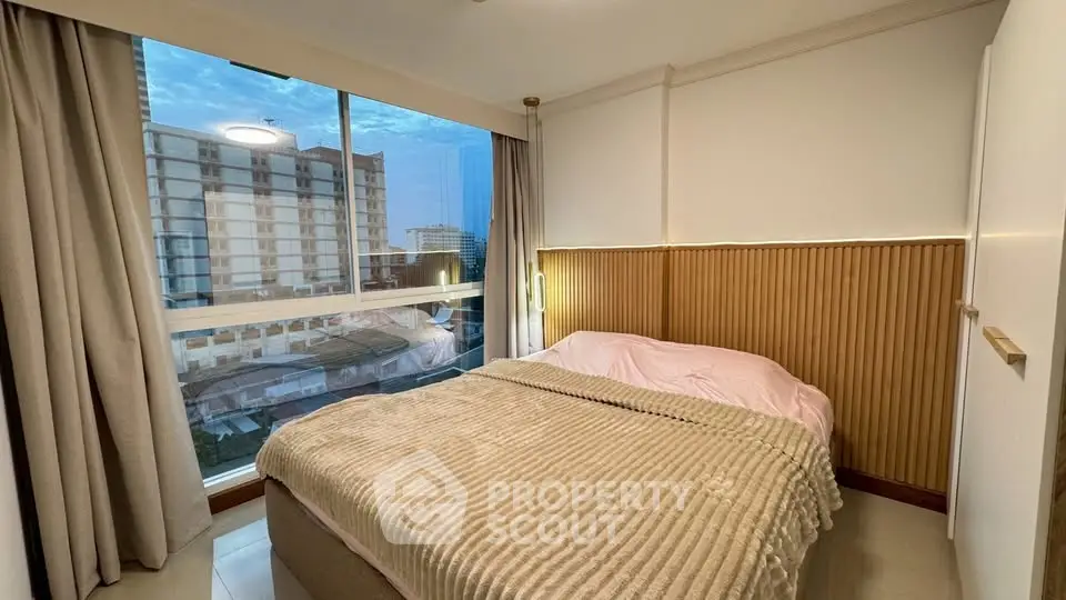 Cozy bedroom with large window offering city view, featuring modern decor and comfortable bedding.