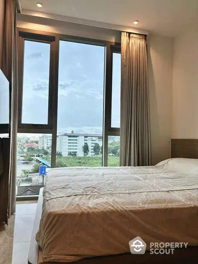 Cozy bedroom with large windows offering a stunning city view, perfect for relaxation and comfort.