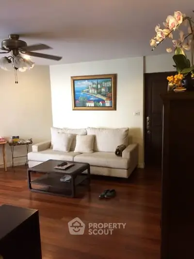 Cozy living room with wooden flooring, elegant sofa, and ceiling fan in a modern apartment.