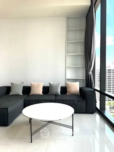 Modern living room with sleek black sofa, large windows, and city view.