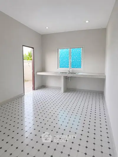 Spacious kitchen with tiled floor and large window, offering ample natural light and minimalist design.