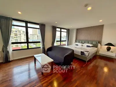 Spacious bedroom with large windows and city view, featuring elegant hardwood floors and modern furnishings.