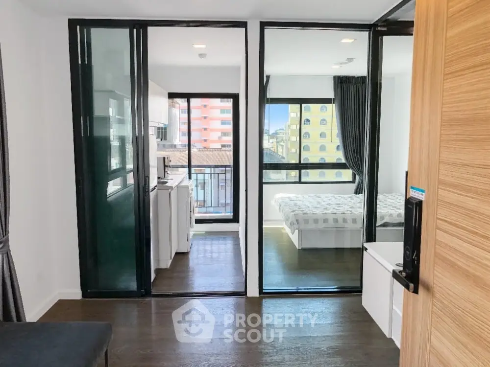 Modern apartment with open layout, featuring a kitchen and bedroom with large windows and city views.
