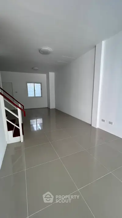 Spacious empty room with glossy tiled flooring and staircase, ideal for customization.
