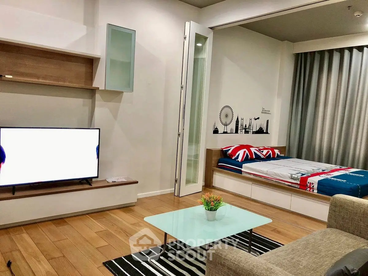 Modern living room with stylish decor and cozy sleeping area, featuring wooden flooring and sleek furniture.