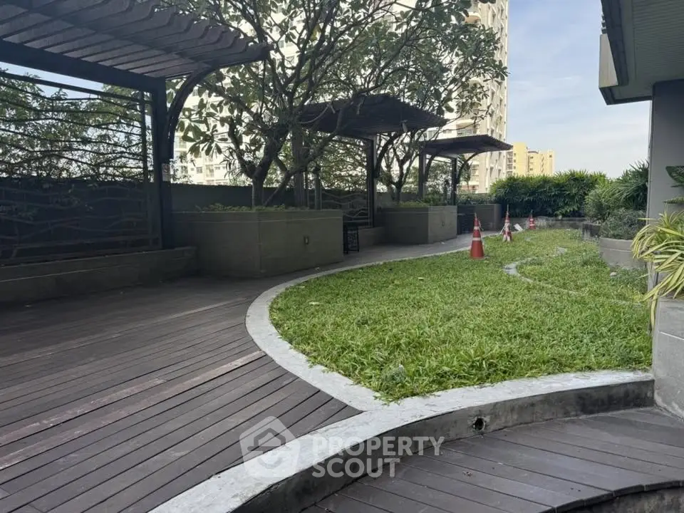 Serene garden area with wooden deck and lush greenery in modern residential complex.