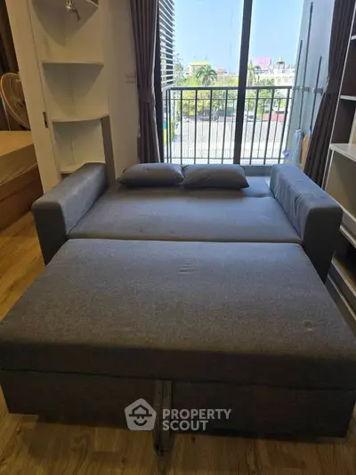 Modern studio apartment with convertible sofa bed and balcony view.