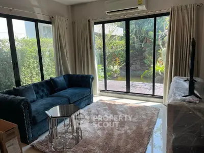 Charming living room with plush sofa, large windows, and garden view, perfect for relaxation.