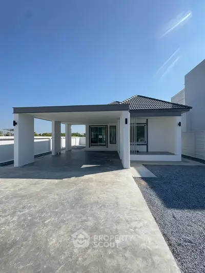 Modern single-story house with spacious driveway and sleek design under clear blue sky.
