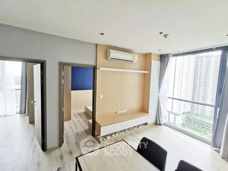 Modern apartment interior with large windows and city view, featuring a stylish living area and bedroom entrance.