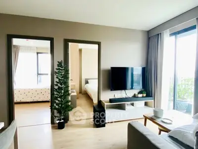 Modern living room with TV, cozy seating, and view into bedrooms, featuring natural light and stylish decor.