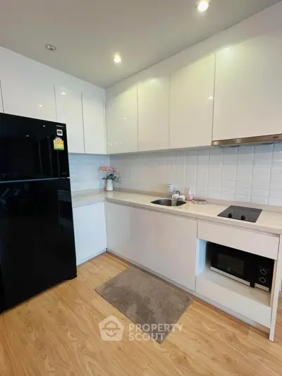 Modern kitchen with sleek white cabinets and black fridge in stylish apartment