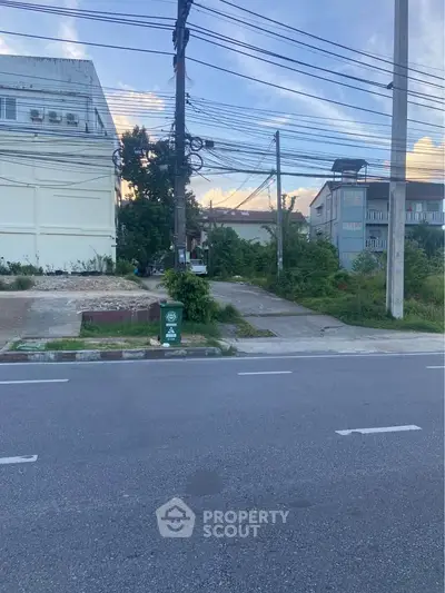 Street view of residential area with buildings and greenery, showcasing potential real estate development.