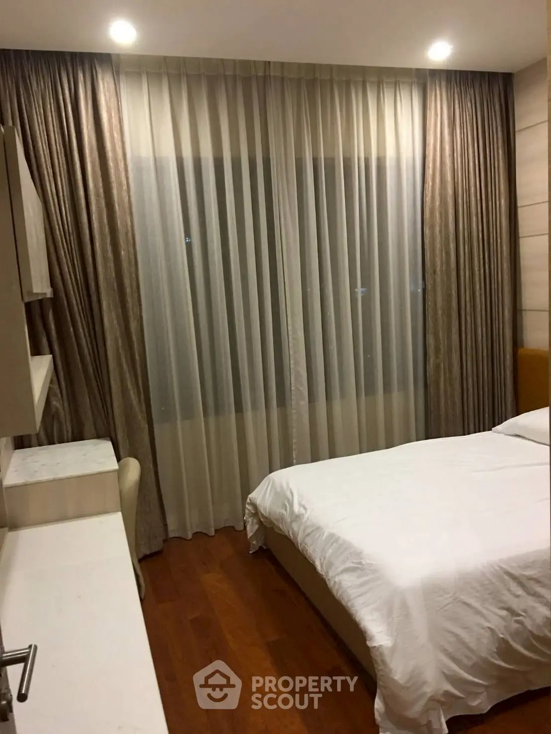 Cozy bedroom with elegant curtains and wooden flooring, perfect for relaxation.