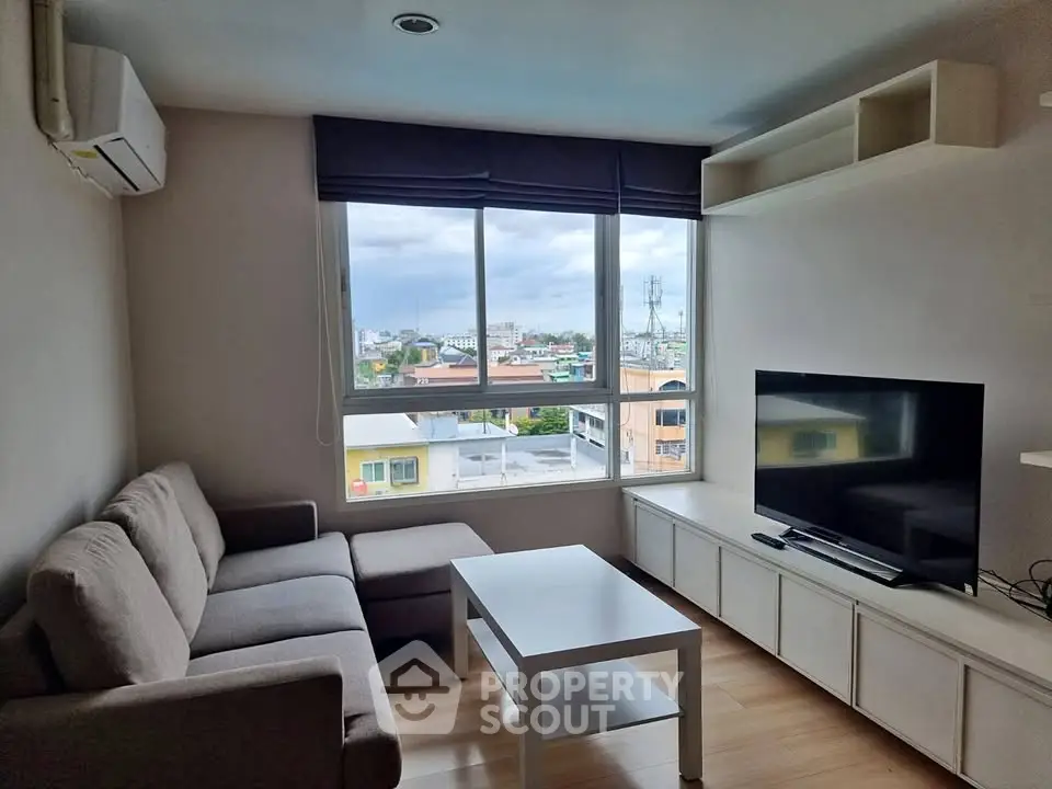 Cozy living room with large window offering city views, modern sofa, and flat-screen TV.