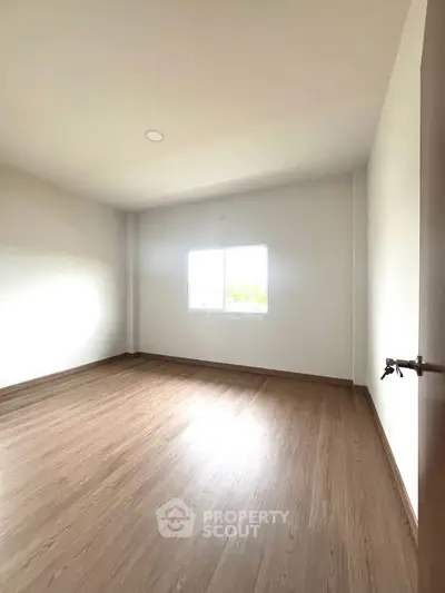Spacious empty room with wooden flooring and bright window, perfect for customization.